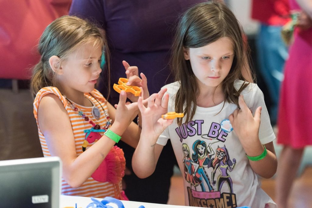 Girls at Maker Faire Detroit check out custom fidget spinners made by Kinvert students using our 3D Printer