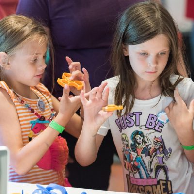 Girls at Maker Faire Detroit check out custom fidget spinners made by Kinvert students using our 3D Printer